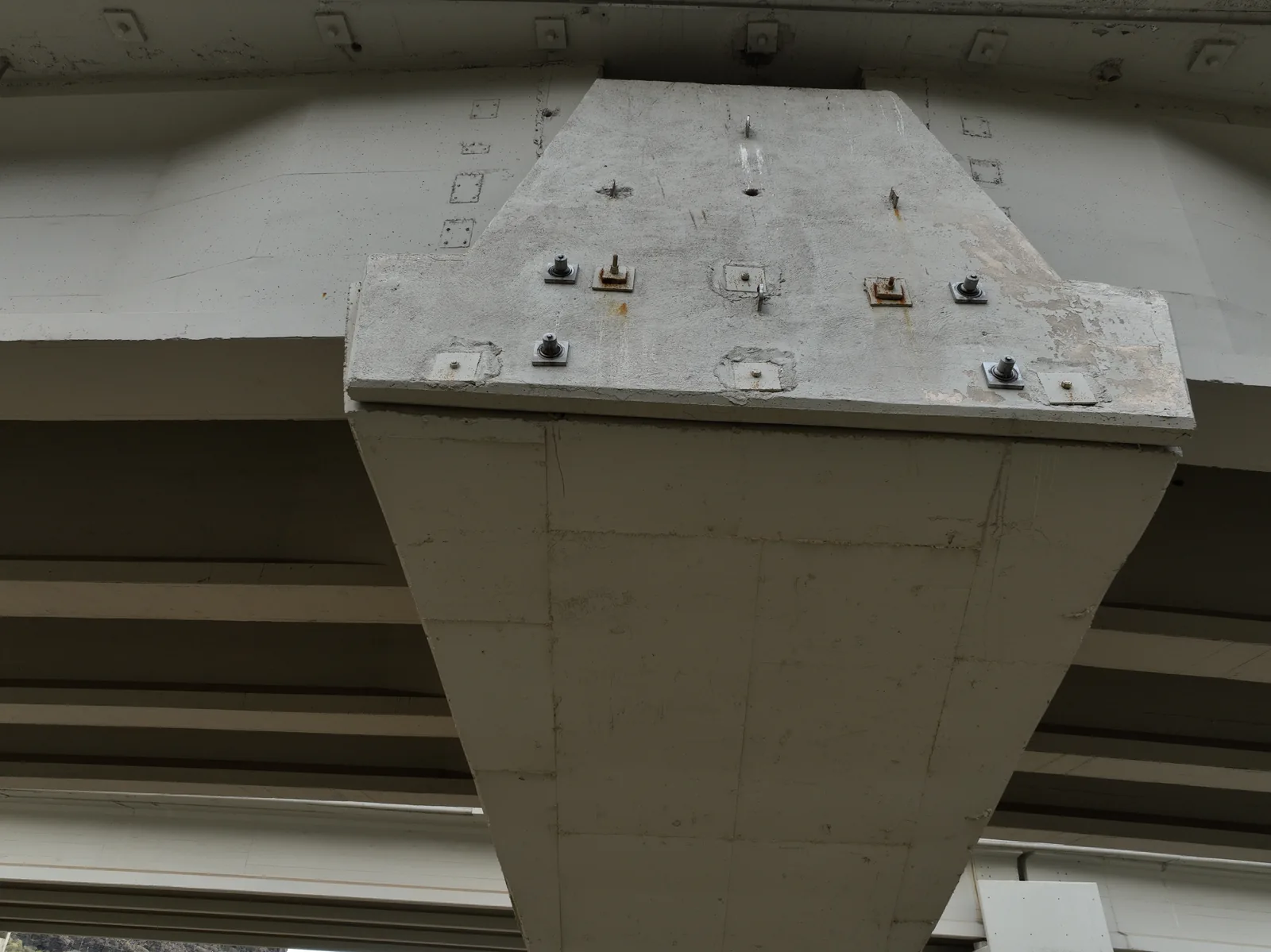 Cabeza de pila de un viaducto vista desde abajo: los apoyos atornillados del tablero, con regueros de oxido alrededor de los anclajes